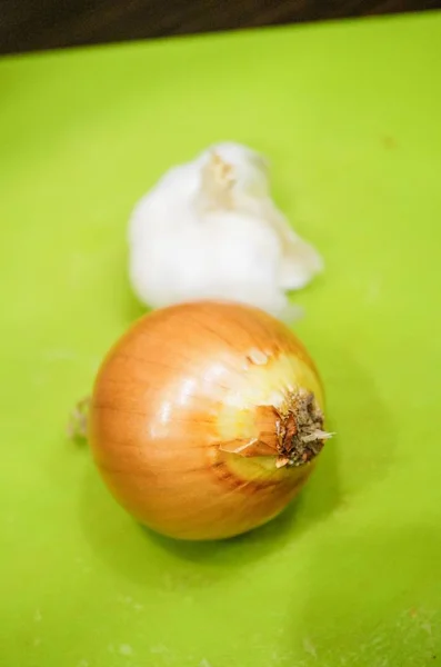 Nahaufnahme einer ganzen und ungeschälten weißen Zwiebel und eines halben Knoblauchkopfes auf einem Schneidebrett — Stockfoto