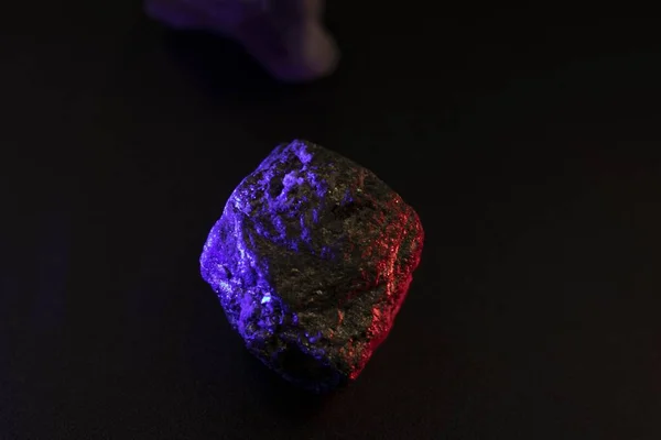 Foto de cierre de una piedra mineral con tintes de color morado y rojo sobre fondo negro. — Foto de Stock