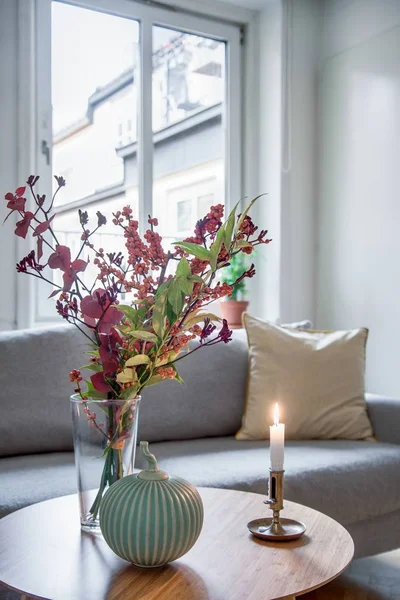 Foto vertical de flores en un jarrón y una vela en una mesa cerca de un sofá. —  Fotos de Stock