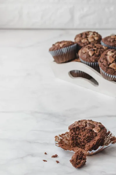 Schokoladenmuffins in einem Tablett serviert. Einer von ihnen gebissen und isoliert auf weißem Marmorhintergrund. — Stockfoto