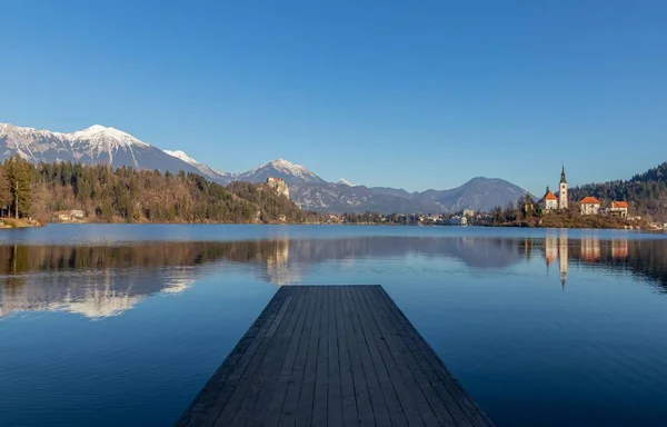 Réflexion des montagnes et des vieux bâtiments du lac avec au premier plan une jetée en bois — Photo