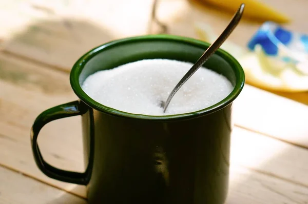 Closeup of sugar with a spoon in a green mug on the table under the lights — Stock Photo, Image