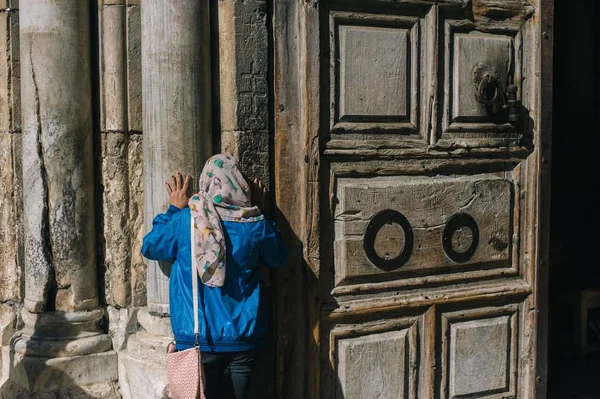 Γυναίκα με μαντίλα που αγγίζει την ξύλινη πόρτα ενός ιστορικού θρησκευτικού κτιρίου — Φωτογραφία Αρχείου