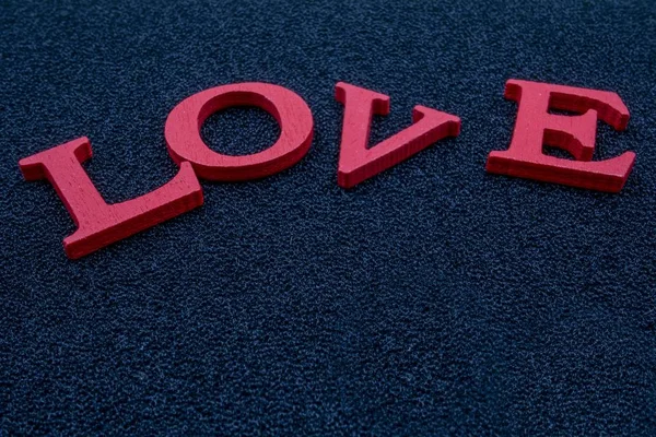 Primo piano sparato di blocchi di legno lettera rossa che indica "amore" su un tappeto blu — Foto Stock