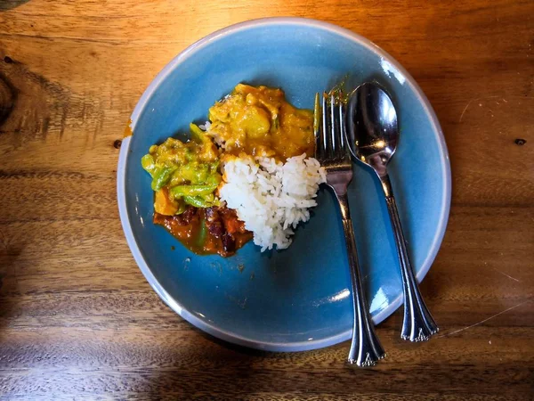 Κάτοψη στιγμιότυπο ινδικού κάρυ και ρυζιού σε μπλε πιάτο με κουτάλι και πιρούνι σε ξύλινο τραπέζι — Φωτογραφία Αρχείου
