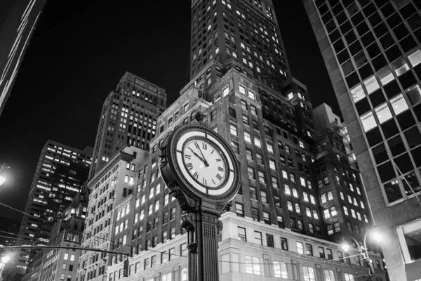 Grayscale shot of clock on the sidewalk in the middle of buildings — Stock Photo, Image