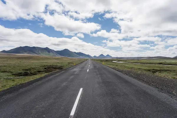 Route vide au milieu de champs herbeux avec des montagnes au loin — Photo