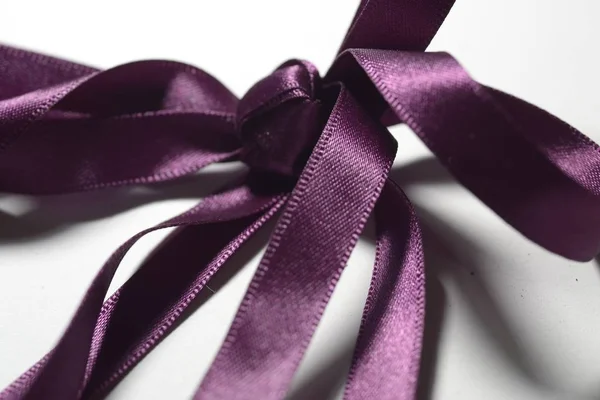 Ujęcie zbliżeniowe fioletowej wstążki przywiązanej do kokardy z białym tłem — Zdjęcie stockowe