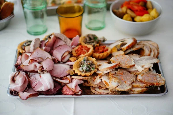 Piatto di metallo pieno di snack e antipasti su un tavolo ricoperto da una tovaglia bianca — Foto Stock