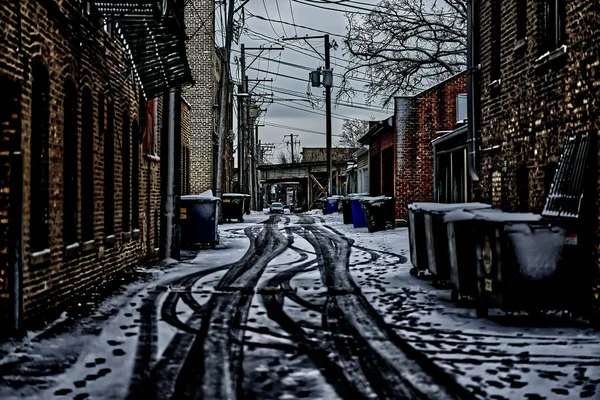 Trilhas de carro na neve com lixeiras entre os edifícios — Fotografia de Stock