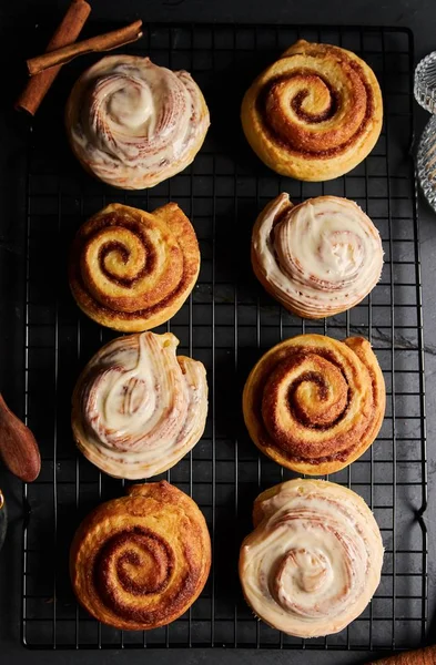 A vertical shot of delicious Cinnamon Rolls with White Glaze on a black table