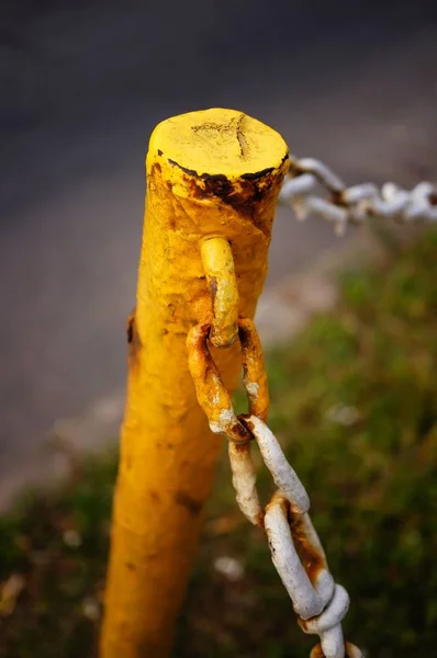 Close-up shot van een licht roestige gele paal met kettingen bevestigd in een park op een bewolkte dag — Stockfoto