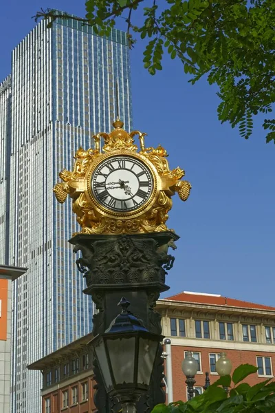 Vertical shot of a golden watch behind a skyscraper — Stock Photo, Image