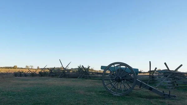 Стара гармата в полі, оточеному зеленню і парканом під сонцем і синім небом. — стокове фото