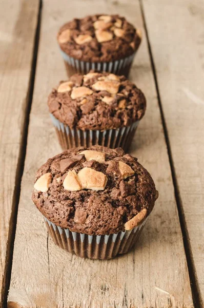 Imagen vertical de tres muffins de chocolate alineados sobre un fondo de madera.. — Foto de Stock
