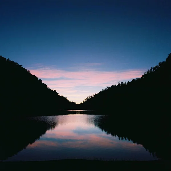 Sylwetki Drzew Wzgórzach Odbitych Jeziorze Zachodzie Słońca — Zdjęcie stockowe