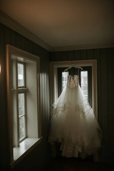 Vertikal bild av en vacker bröllopsklänning hängande nära ett fönster i ett rum — Stockfoto