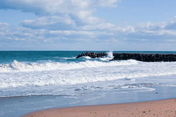 Fotografie relaxačních vln oceánu na břehu s kamenným dokem pod zataženou oblohou — Stock fotografie