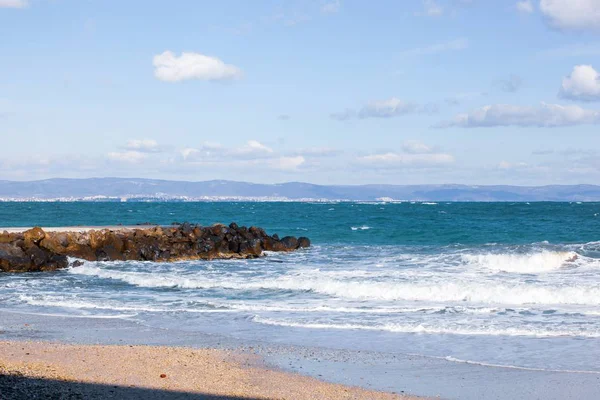 Foto de relajantes olas oceánicas en la orilla con muelle de piedra bajo cielos nublados — Foto de Stock