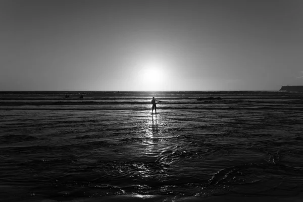 Photographie en niveaux de gris d'une personne se tenant dans l'eau au loin — Photo