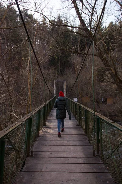 Mögötte egy vörös kalapos lány sétál a fa hídon, csupasz fákkal körülvéve. — Stock Fotó