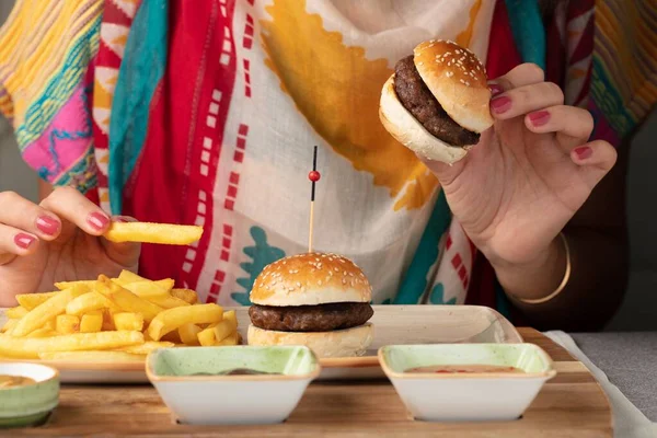 A closeup shot of a person eating small hamburgers and fries