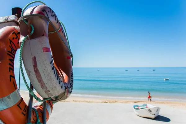 Bouée de sauvetage suspendue à un poteau avec une plage floue à l'arrière-plan — Photo