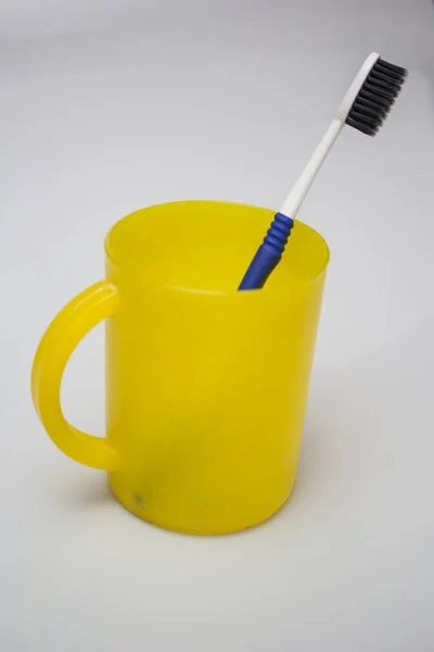 Scatto verticale di uno spazzolino da denti in una tazza di plastica gialla con un colore bianco sullo sfondo — Foto Stock