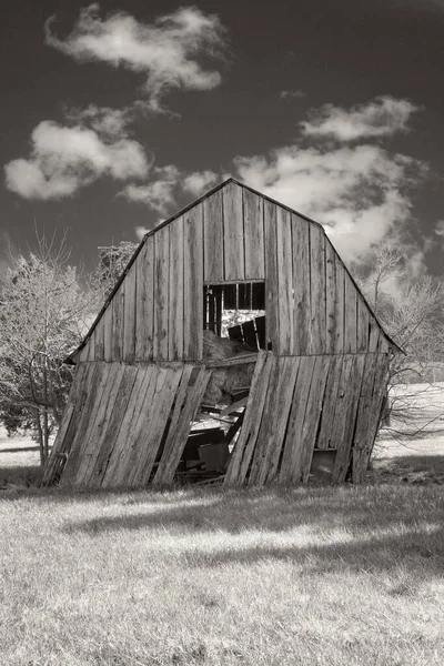 在乌云密布的天空下 一个古老的木制谷仓侧卧在一边的黑白垂直镜头 — 图库照片