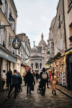 PARIS, FRANCE - Dec 26, 2019: People walking a street in Montmartre with the Sacr Coeur in the background  clipart