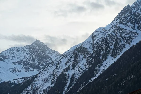 Bellissimo scatto di una ripida montagna ricoperta di neve bianca con un cielo nuvoloso sullo sfondo — Foto Stock