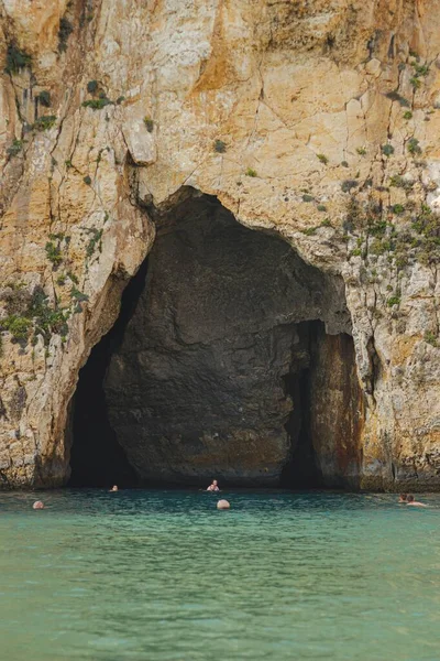 Tiro Vertical Caverna Penhasco Perto Oceano Com Pessoas Nadando — Fotografia de Stock