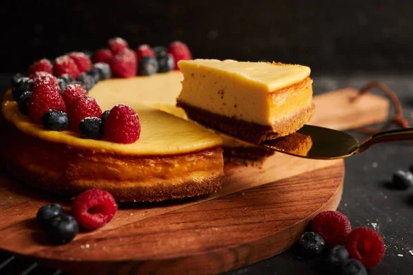 黒を基調とした木の板の上にベリーのあるチーズケーキとスライス — ストック写真