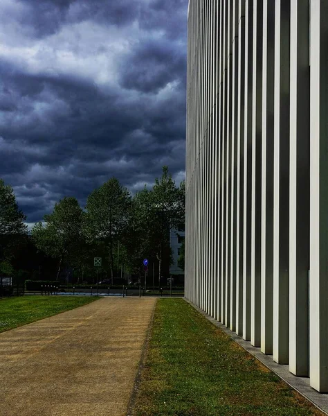 Függőleges felvétel a felhős szürke égboltról egy modern építészeti épülettel az oldalán — Stock Fotó