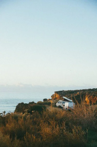 Вертикальный Снимок Белого Фургона Возле Скалы Моря Днем — стоковое фото