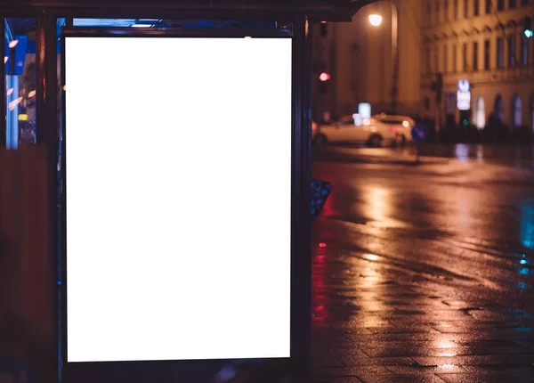 Bus stop with blank white space for your ad. Free copy space on illuminated bus stop during rainy night in urban european city.