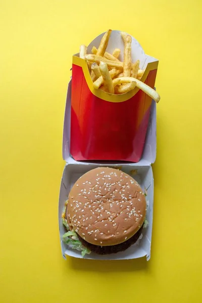 A burger and fries in a box on the yellow table under the lights