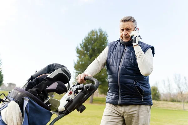 A man standing in the golf field and talking on the phone