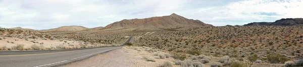 高い岩場に囲まれた茂みに覆われた砂漠地帯での空の道のパノラマショット — ストック写真