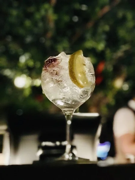 背景がぼやけているワイングラスに氷とレモンとドリンクの垂直ショット — ストック写真