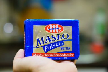 POZNAN, POLAND - Feb 20, 2020: Polish Mlekovita Maslo Polskie butter packed in paper on a open hand in soft focus background. clipart