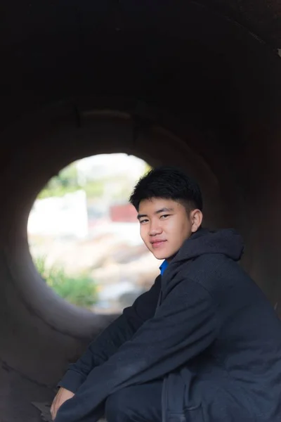 一位年轻英俊的亚洲男子 头戴头巾 面带微笑 坐在水泥管子里 — 图库照片
