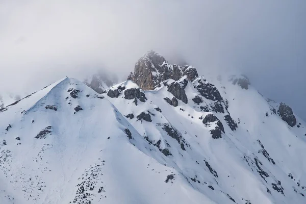 暗い灰色の空の下で雪に覆われた山の岩のピーク — ストック写真