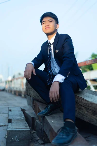 Mladý Asiat Obleku Sedí Hromadě Klád Dívá Jinam Sluncem Tváři — Stock fotografie