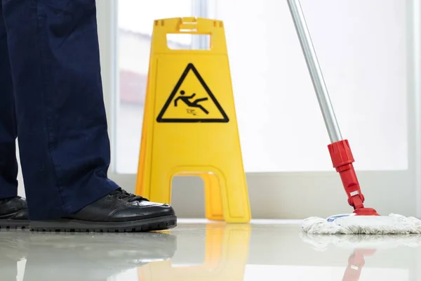 床を掃除する者の低い角度の閉鎖黄色の注意湿った床の標識の近くのモップで — ストック写真