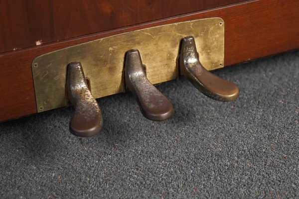 A closeup of old rusty piano pedals under the lights