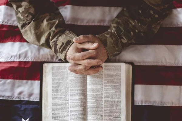 An American soldier mourning and praying with the American flag and the Bible in front of him