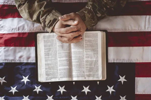 An American soldier mourning and praying with the American flag and the Bible in front of him