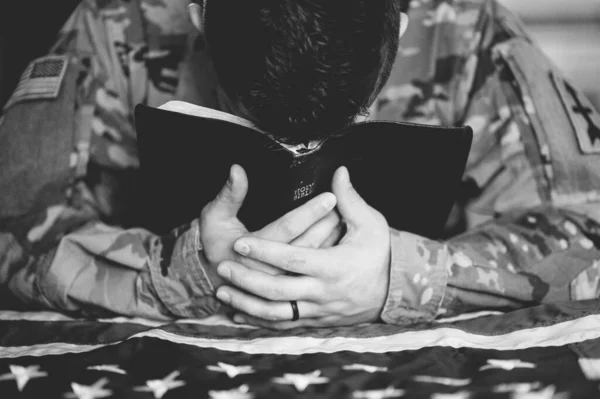 A greyscale shot of an American soldier mourning and praying with the Bible in his hands