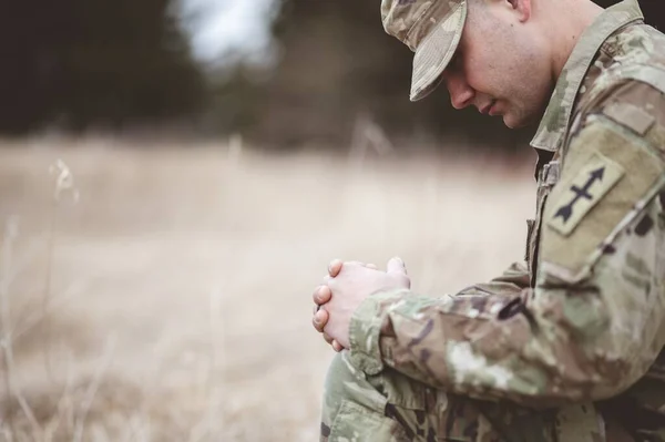 一个年轻士兵跪在干枯的草地上祈祷的浅浅的镜头 — 图库照片